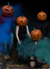 Halloween celebration featuring creatively carved pumpkins on a dark, smoky autumn night with friends in spooky attire