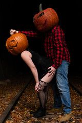 Couple in Halloween costumes explore a spooky train track while wearing pumpkin heads at night during autumn celebration