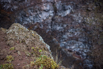 Focused close-up of Rugged Volcanic Rock Cliff with Green Vegetation and brown soil overshadowing...