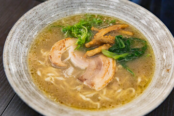 Japanese ramen with grilled pork slices, golden broth, spinach, mushrooms and green onions in ceramic bowl served on dark wooden table