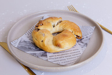 Semi circle twisted bread roll with visible dried cranberries, golden crust, soft texture, placed on printed liner and neutral ceramic plate