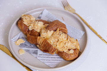 Almond croissant with crispy golden layers and sliced almonds scattered on top, served on ceramic plate lined with printed paper