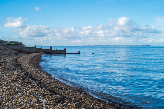 The pebble beach shoreline and a wooden groyne in Tankerton, Whitstable on a bright, blue autumn day. The Isle of Sheppey can be seen on the horizon.