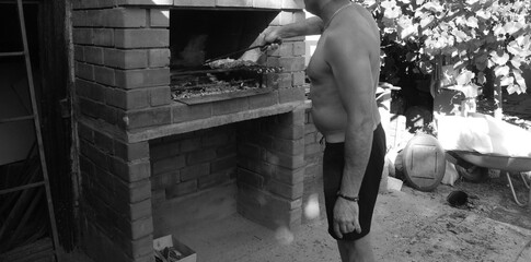 A man is standing near the barbecue and frying shalyk in summer, hands and food are visible