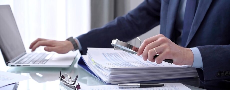 Business people wearing blue suits are reviewing financial data in office. Male auditor is using a magnifying glass. Audit and taxes concept