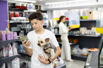 Caring teenage boy visiting pet store with cute little Yorkshire terrier to buy canned dog food for...