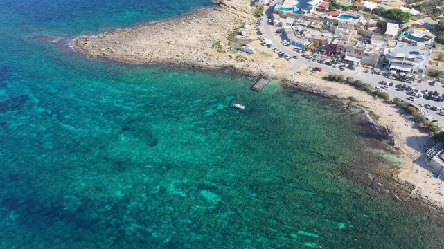 Cinematic drone flight soars over the vibrant turquoise waters of Bahar ic-Caghaq, revealing the rugged limestone coastline and crystal-clear Mediterranean sea in Malta