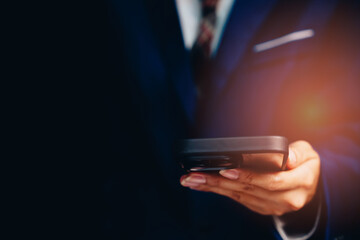 Professional man in business attire using smartphone in dark setting, showcasing modern communication and technology concepts