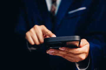 Businessman in Suit Using Smartphone with Focus on Hands and Device Against a Dark Background