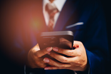 Professional man in a suit holding a smartphone with a blurred background and soft lighting effect in a modern setting