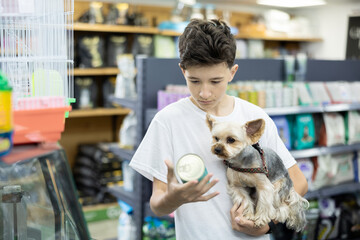 Focused preteen boy carefully selecting quality canned dog food for beloved Yorkie in pet store,...