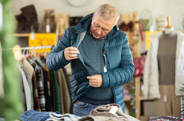 Mature man trying on a warm down jacket near the counter in the Christmas shop. Buying outerwear at the New Years sale