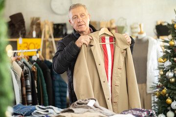 Elderly man chooses raincoat in a clothing store