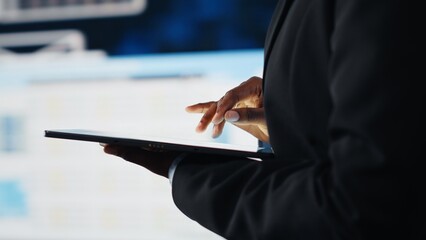 Close up of businesswoman using tablet to compare company KPIs data on digital videowall before making decisions. Entrepreneur analyzing key performance indicators using device app
