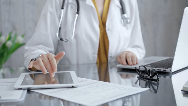 Doctor woman using tablet on the glass desk in medical office. Close-up of a doctor's hands interacting with a touch pad in clinic. Medicine and health care - Powered by Adobe