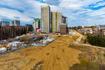 Modern residential buildings rise high above a large, active construction site. This urban development scene captures ongoing work and new architecture under a partly cloudy sky
