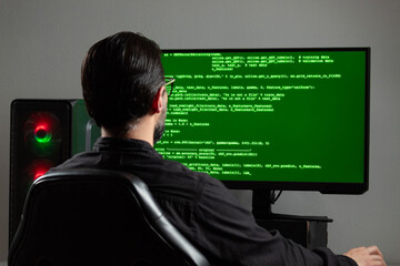 a man backward watching a computer monitor with a green html programming code on the screen