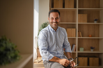 Smiling man holding glasses at home office