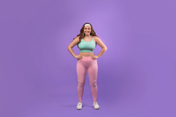 Cheerful plus size woman athlete stands confidently in sportswear against a purple background. She shows a positive attitude, ready for workout and fitness motivation focusing on exercise.