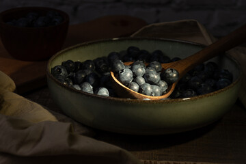 Wooden spoon with blueberries illuminated by a ray of sunlight in a bowl.