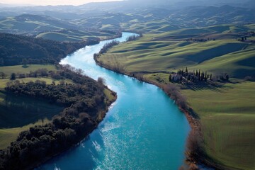 Fototapeta premium Aerial view showcases a winding river flowing through rolling green hills under soft, diffused