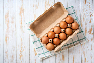 chicken eggs in a carton box on a light kitchen table, selective focus, top view.