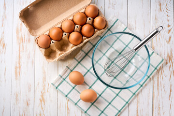 beat eggs with egg whisk in a glass bowl on a kitchen table, top view. Cooking scrambled fresh eggs for breakfast.