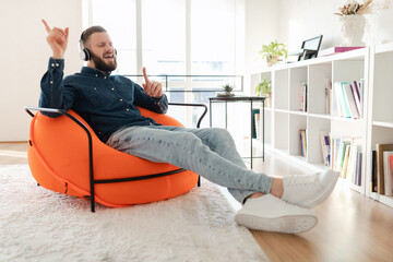 A man listens to music through headphones while sitting comfortably in an orange bean bag chair....