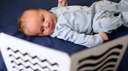 A baby boy looks at black and white high-contrast pictures for newborns. The child is 1.5 months old.