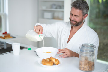 Man eats breakfast in the kitchen. Guy enjoys fresh food at the kitchen table in the morning. A man eats cereal and fruit in the kitchen. Man eating healthy food in the kitchen.