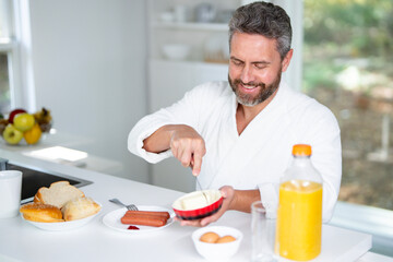 Happy man eating morning breakfast. Healthy food in kitchen for aged mature man. Portrait of senior man at kitchen and eat lunch. 50s man eating breakfast in cozy kitchen at home.