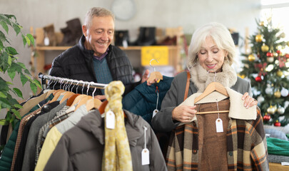 Fototapeta premium Glad old-aged spouses looking for winter outwear in retail outlet during X-mas sell-out season