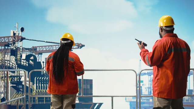 Offshore platform engineer reports operation status using walkie talkie, following safety protocols. African american man in charge of drilling rig communications doing checkup on equipment, - Powered by Adobe