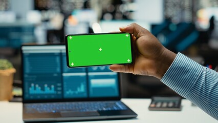African american guy looks at mockup display on phone at night, solving business tasks after hours. Office consultant working on project development, meeting targets and goals.
