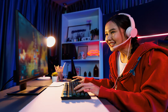 Host channel of young beautiful Asian gaming streamer playing fighting Moba at battle arena game on pc screen with multiplays, wearing pastel headphone at neon digital light modern room. Stratagem.