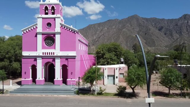 Aerial video passing willow trees to reveal the pink Our Lady of Candelaria Church in Copacabana, Catamarca. 