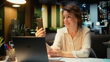 Entrepreneur joining online meeting on phone at night in office, maintaining eye contact with the webcam. Executive manager focused on communication, participating in a collaborative chat. Camera A.