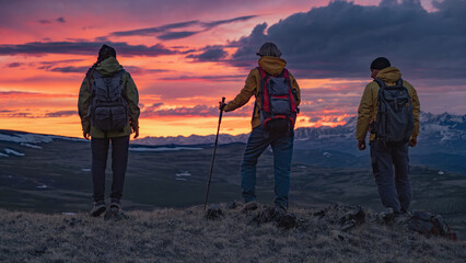 Travelers in bright clothes and with backpacks on their backs are standing on a high mountain...