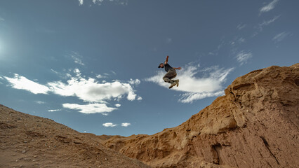 A man jumps from a high mountain against a blue sky. A jump from a cliff in a canyon.