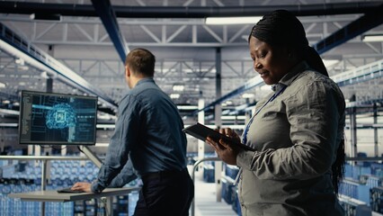 Data center employee monitoring infrastructure processes, reviewing operational metrics. Server room IT worker reviews high tech infrastructure equipment rigs reports during inspection, camera A