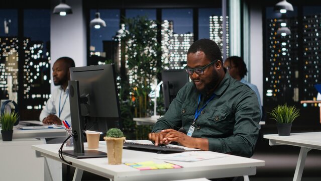 African american office staff leverages analytics and report writing for development and monthly performance results, resources and insights to ensure strategic goals achievement at night.