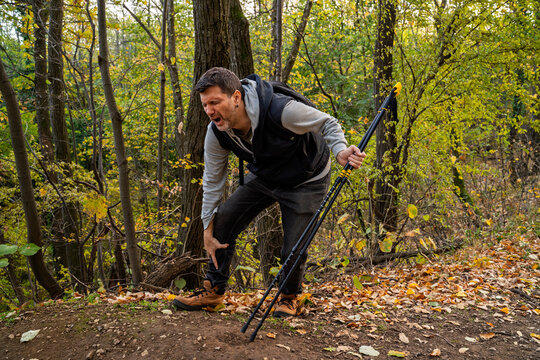 Man hiker with pain grimace on his face, holding hand on knee and ankle, hiking injury, alone in the woods