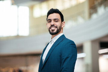 Fototapeta premium A well-dressed man stands confidently in a stylish suit within a contemporary building. Natural light filters through large windows, creating a bright atmosphere.