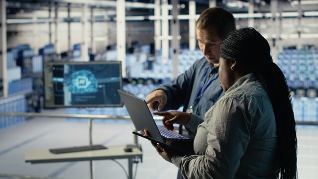 Server room coworkers use laptop to install updates and keep AI systems running. Data center engineering team uses notebook to write code improving infrastructure output, camera B