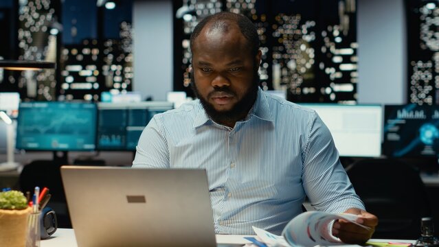 Confident male employee working on a new project task after hours, sitting alone in dark office late at night. Guy fact checking information and monthly agenda for objectives.