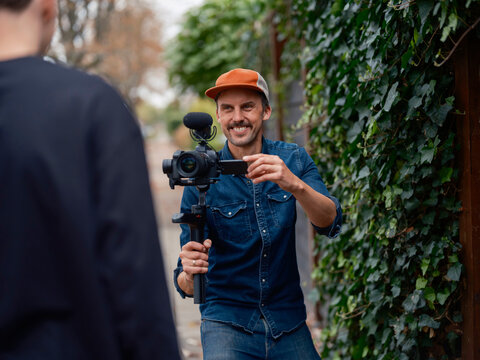 Smiling videographer operating gimbal stabilized camera outdoors, enjoying creative video production work