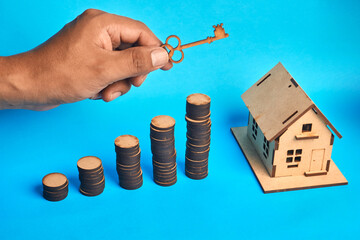 Key over growing coin stacks beside a house model symbolizing real estate investment and home...