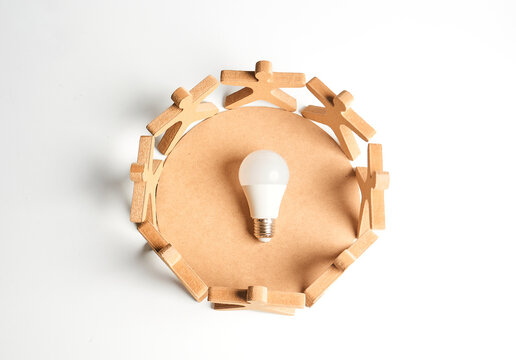 Wooden figures encircling a bulb to represent collective ideas, brainstorming and group innovation powering solutions.

