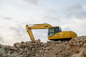 Obraz premium Yellow Excavator On Rocky Pile At Construction Site Under Cloudy Sky For Heavy Duty Earth Moving