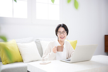 コーヒーを飲みながらリビングでパソコンをする女性　カメラ目線